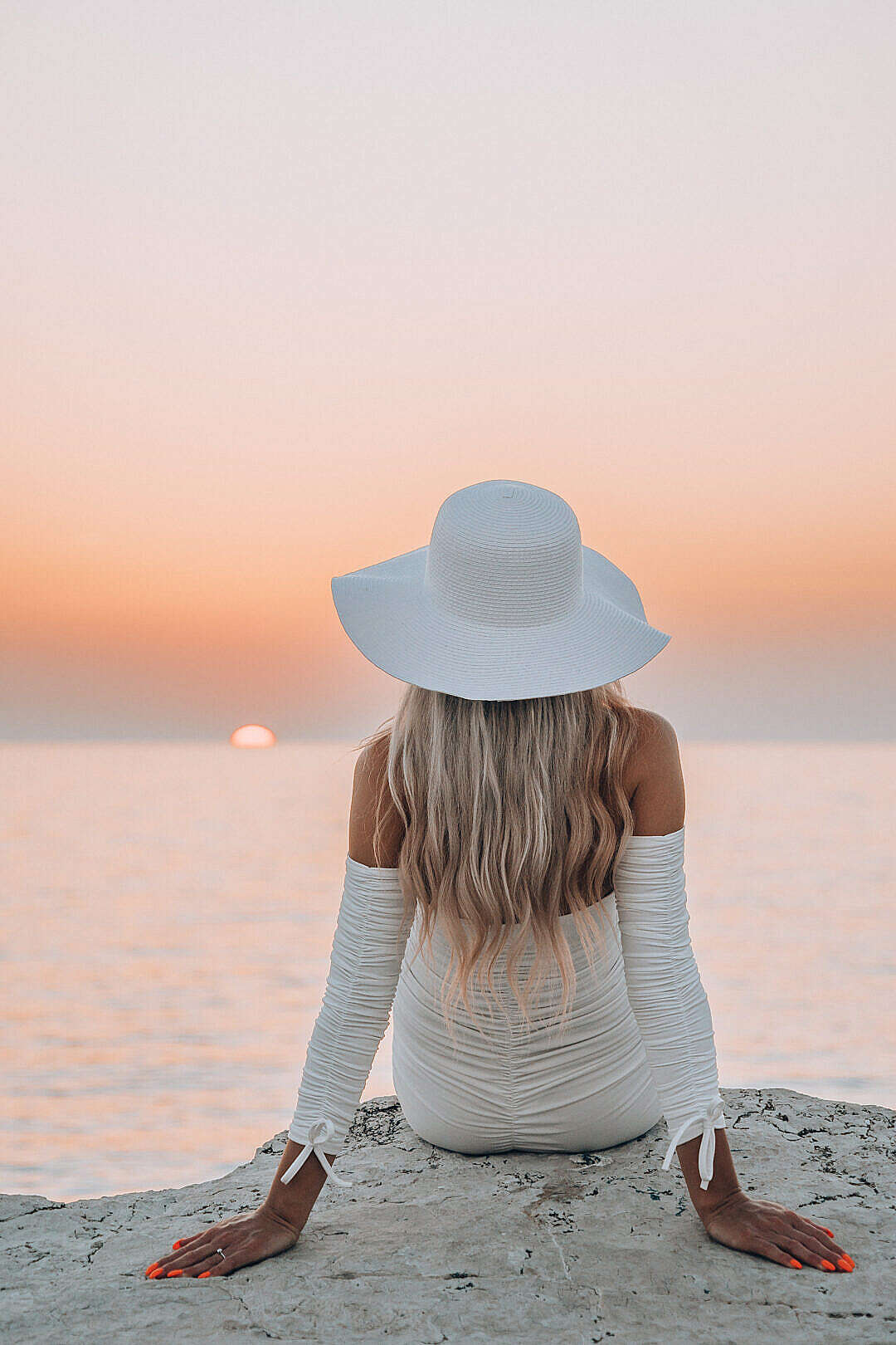 Beautiful Woman in White Hat Sitting on a Rock and Enjoying Sea Sunset
