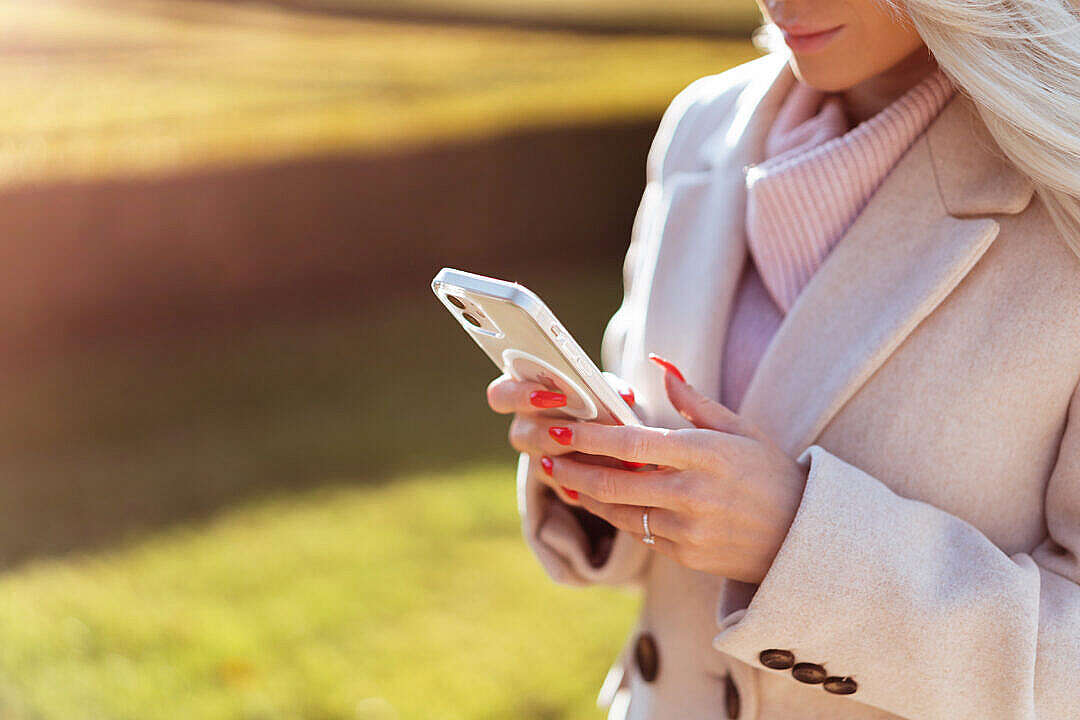 Download Blonde Woman in a Coat Using Her Smartphone Outdoors FREE Stock Photo