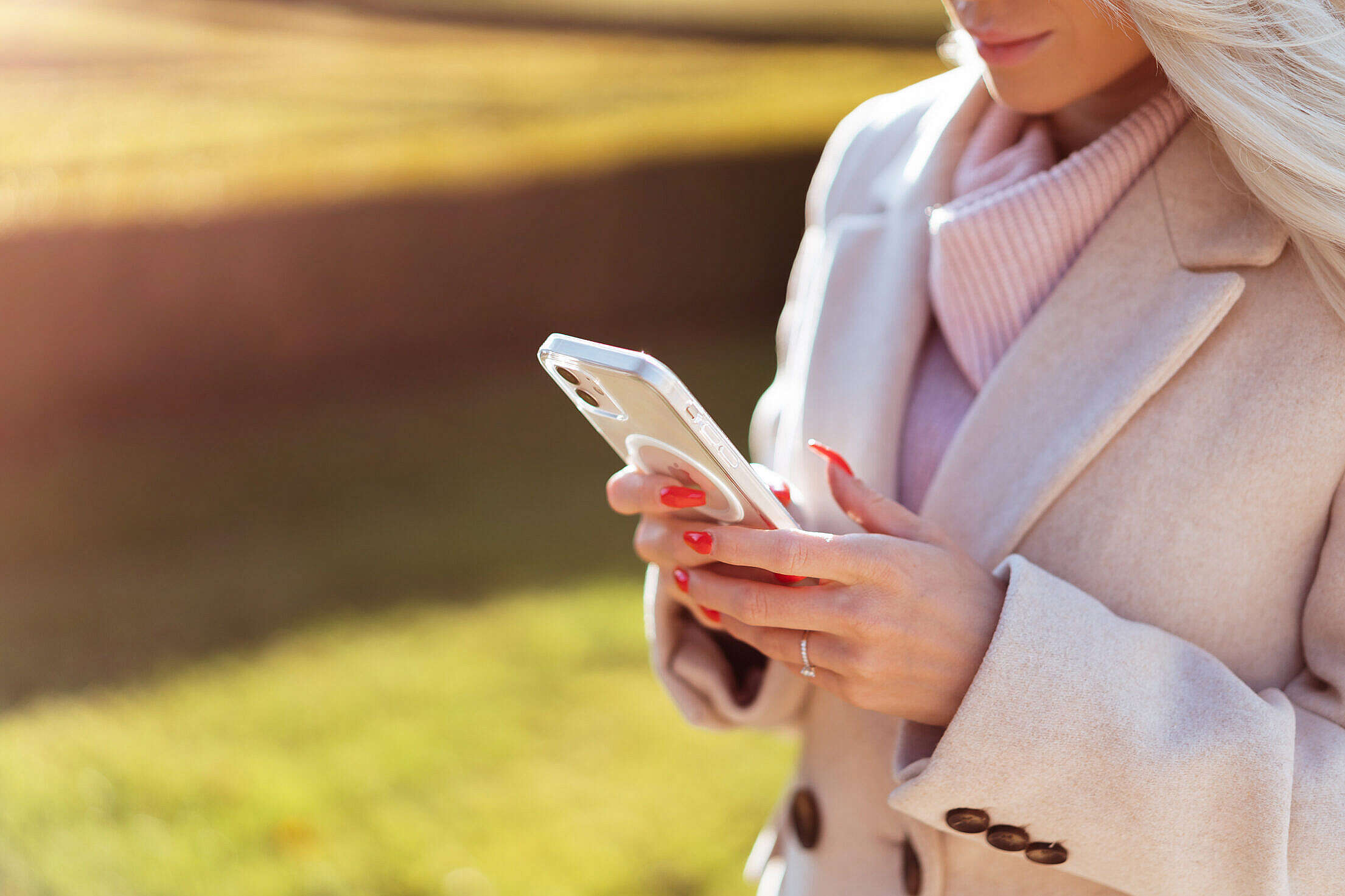 Blonde Woman in a Coat Using Her Smartphone Outdoors Free Stock Photo
