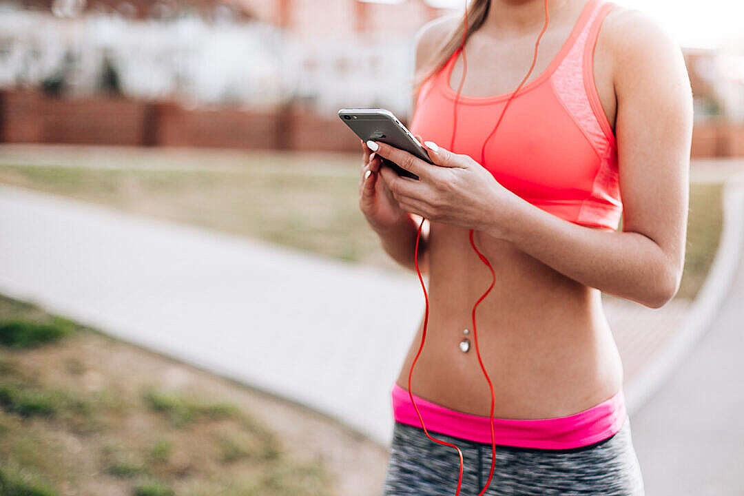 Download Fitness Girl Listening to Streaming Music on Her Phone FREE Stock Photo