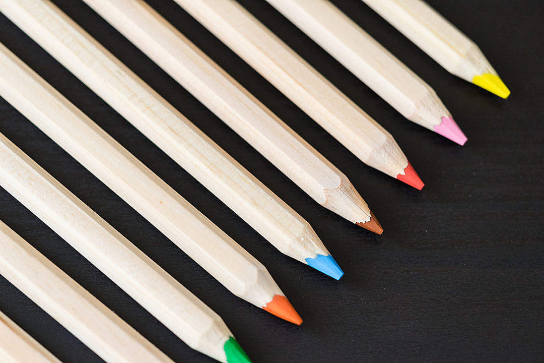 Download Long Colored Pencils in a Row on Black Desk FREE Stock Photo