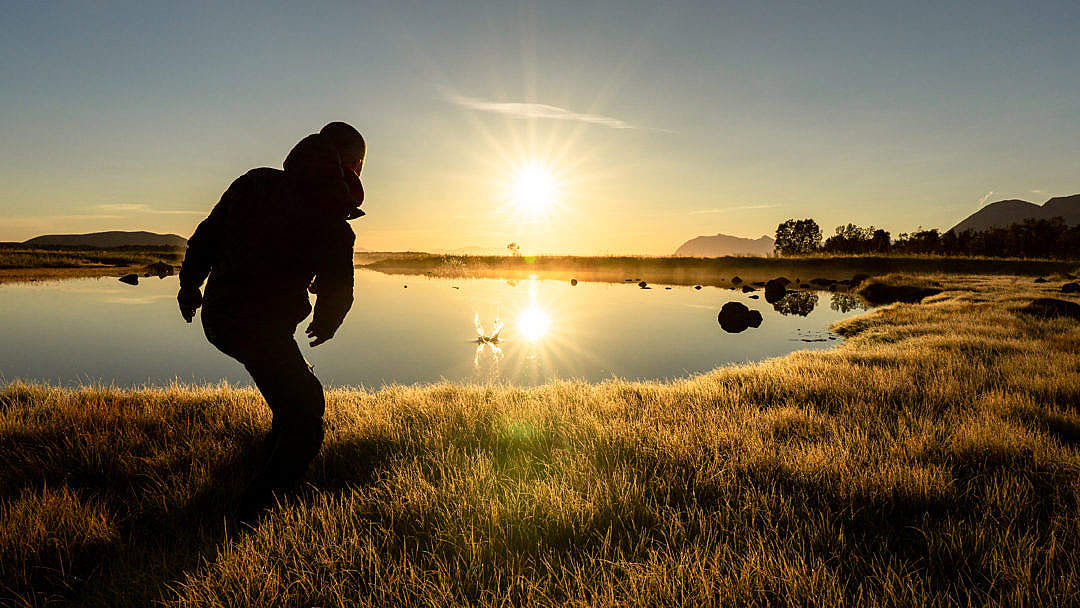 Download Man Throwing a Stone into a Calm Lake During Beautiful Sunrise FREE Stock Photo