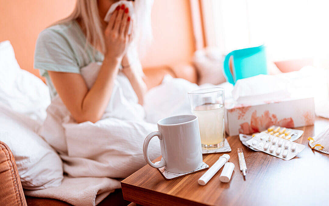 Download Sick Woman Blowing a Nose While Sitting on a Bed FREE Stock Photo