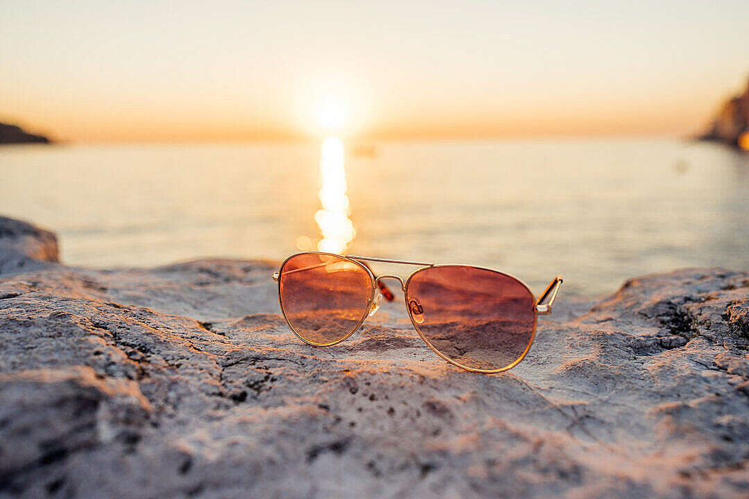 Download Sunglasses on a Stone with Sun Rays During Sunset FREE Stock Photo