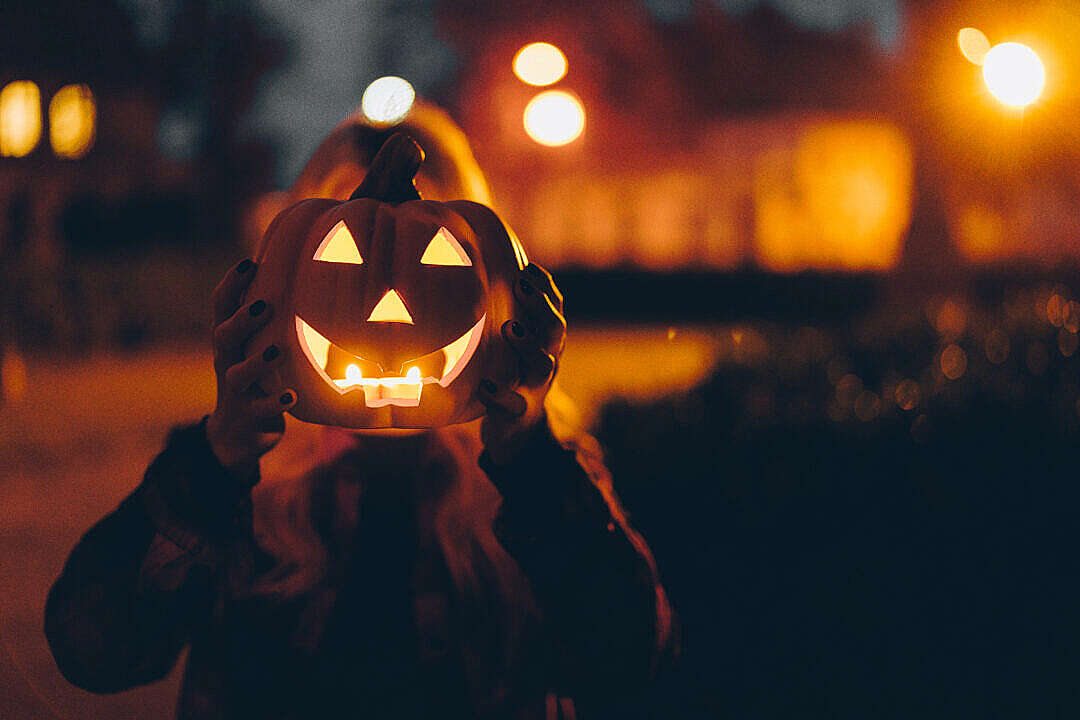 Woman Holding a Halloween Pumpkin in front of her Face at Night