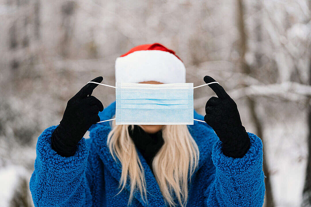 Woman in Santa Hat Holding a Face Mask in Front of Her Face