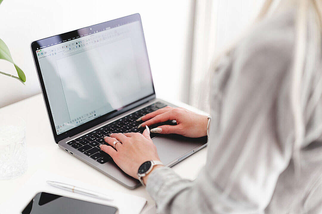 Woman Sitting at Desk and Typing on Laptop