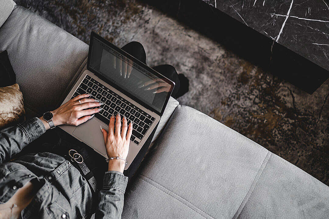 Download Woman Sitting on a Sofa and Typing on Her Laptop FREE Stock Photo