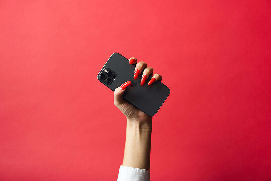 Woman with Red Nails Holding a Smartphone on Red Background