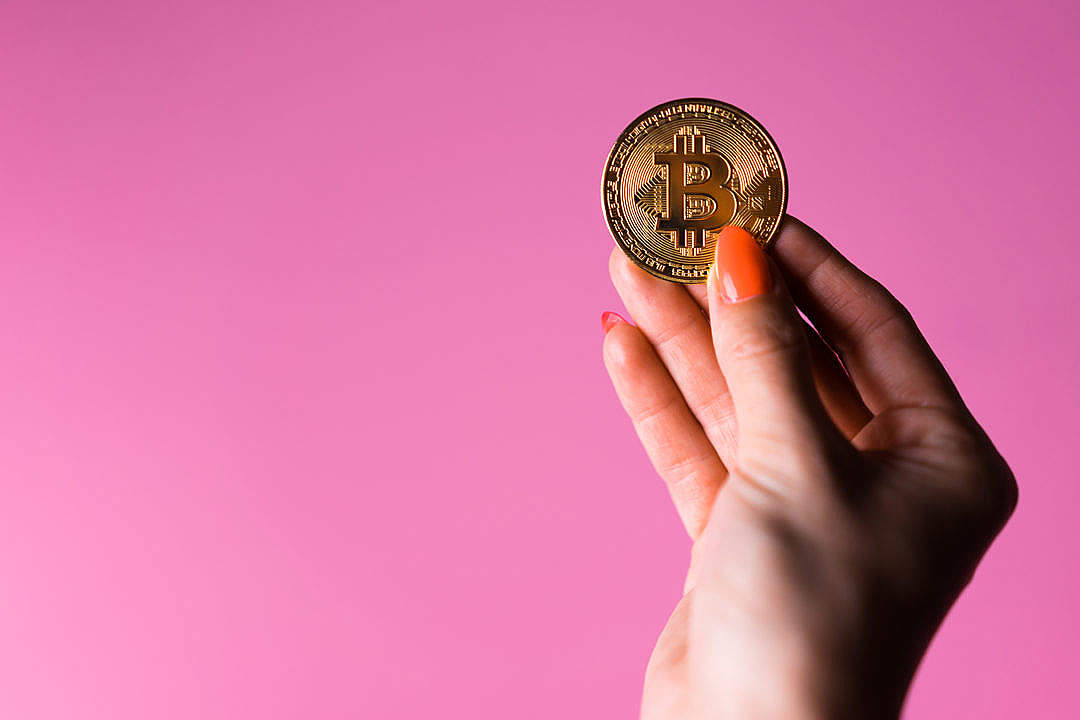 Woman’s Hand with a Glowing Gold Bitcoin on a Pink Background