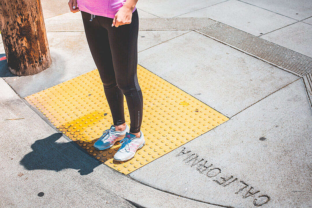 Young Female Jogger Waiting at the Edge of a Zebra Crossing