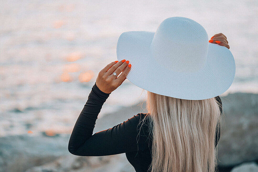 Download Young Woman in White Hat Enjoying Evening Golden Hour by the Sea FREE Stock Photo