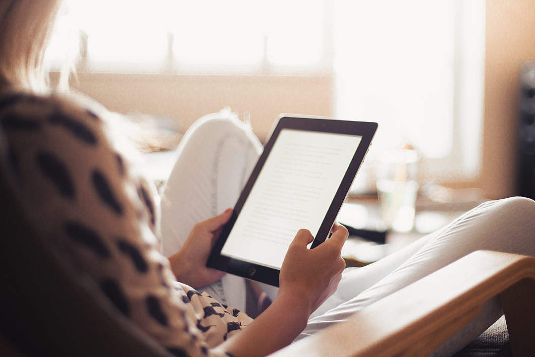 Download Young Woman Reading a Book on Her iPad FREE Stock Photo