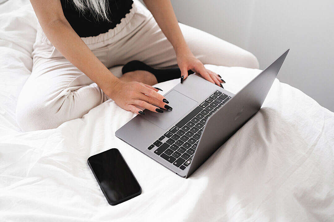 Download Young Woman Working on a Laptop in Bed FREE Stock Photo
